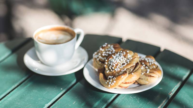 Coffee-and-cinnamon-bun-on-a-green-wooden-table-during-Fika