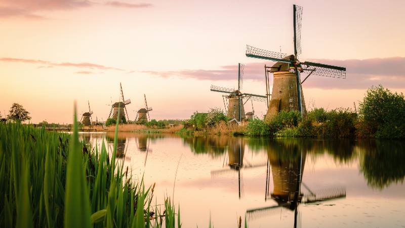A collection of 18th Century traditional Dutch windmills reflected in water at sunrise, at Kinderdijk in South Holland.